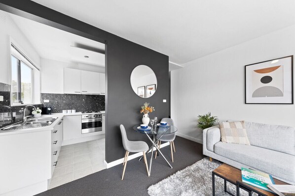 A modern kitchen with white cabinets, a black countertop, and a dining area with a glass table and chairs.