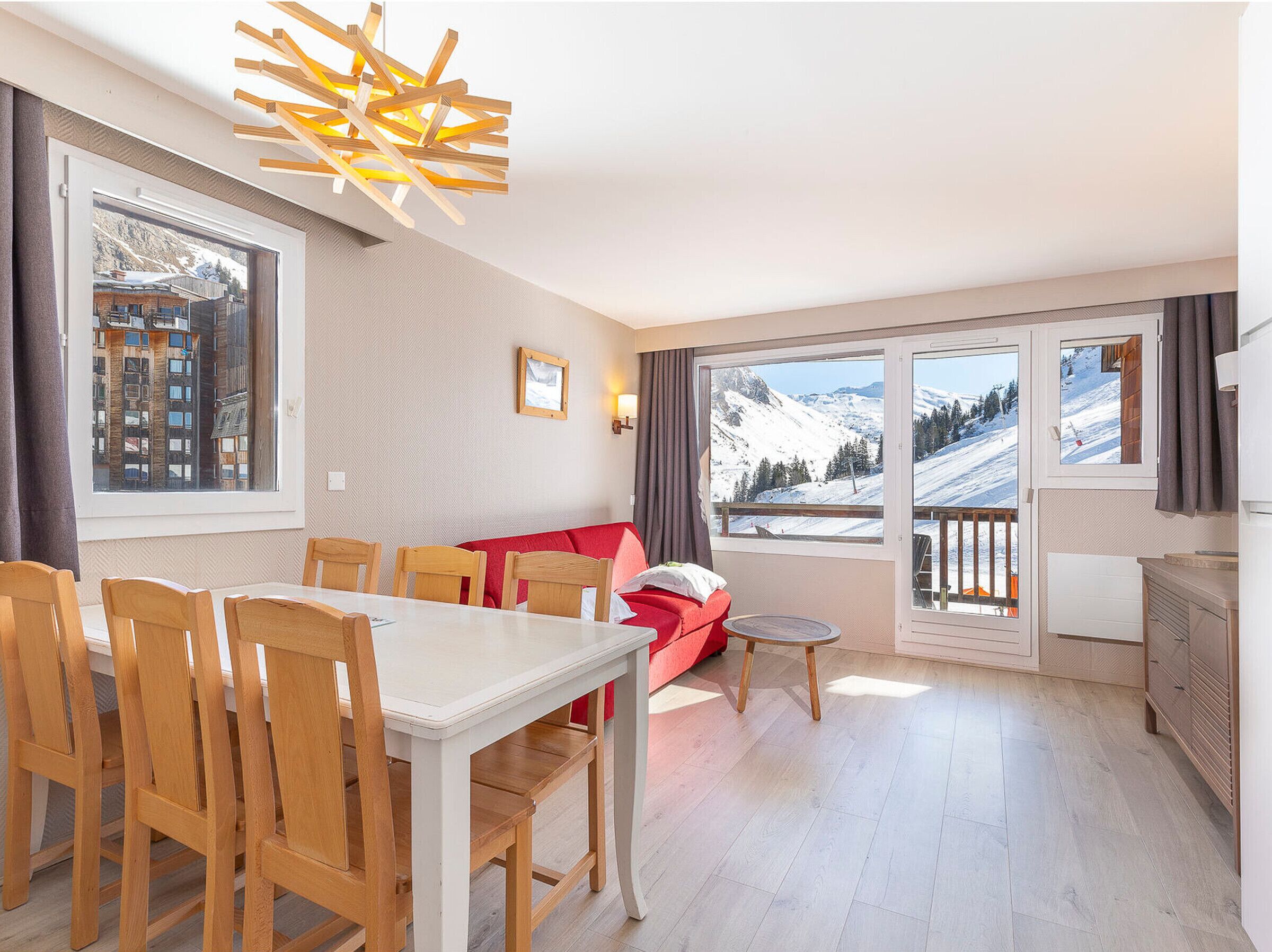 A modern living room with a dining area, large windows with mountain views, and a red sofa.