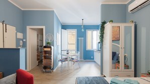 A modern room with a blue wall, a wooden floor, a red chair, a bed with a blue blanket, a white cabinet, and a dining area with a table and chairs. - PETRONIUS HOME STUDIO (Bologna)