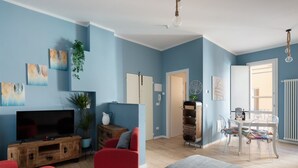 A modern living room with a flat-screen TV, red sofa, and a dining area with a white table and chairs. - PETRONIUS HOME STUDIO (Bologna)