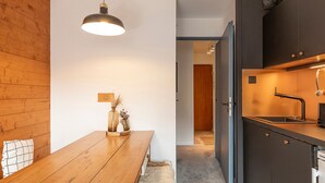 Une cuisine moderne avec des meubles de couleur sombre, une table à manger en bois et un luminaire suspendu.
