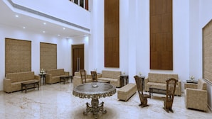 Un hall d’entrée spacieux avec de hauts plafonds, plusieurs coins salon et une grande table ronde au centre.