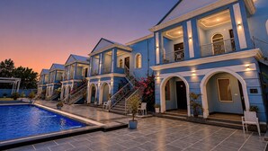 Una casa gran de color blau amb piscina, diversos balcons i una entrada ben il·luminada.