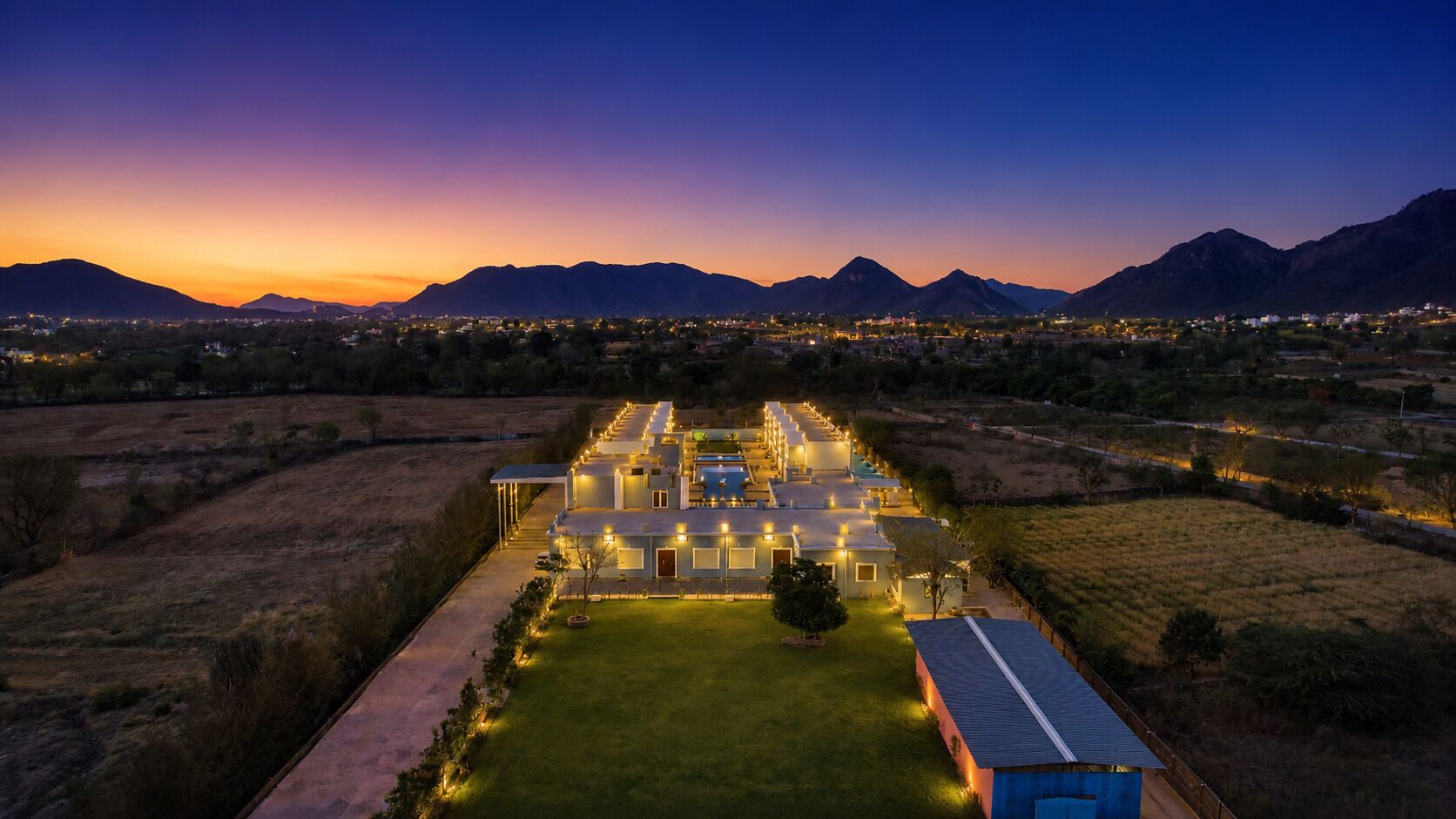 A large, well-lit hotel with multiple buildings and a central courtyard, surrounded by a mountainous landscape.