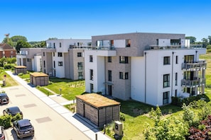 A modern residential building with multiple balconies, a paved driveway, and a well-maintained lawn.