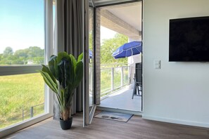 A room with a large window, a potted plant, and a view of a balcony with a blue umbrella.