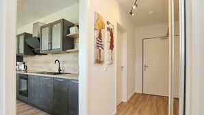 Uma cozinha moderna com armários escuros, uma pia de aço inoxidável e um forno embutido. Há duas pinturas na parede.