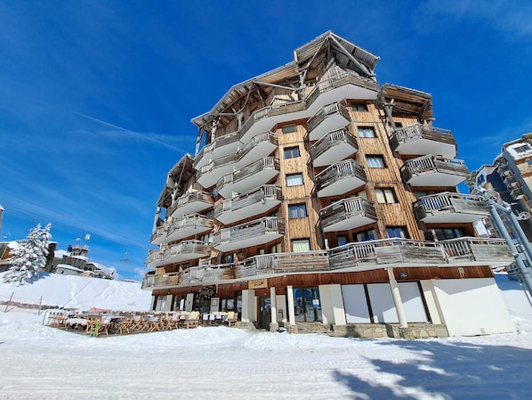 Un hotel de varios pisos con balcones de madera y una pista de esquí al fondo.