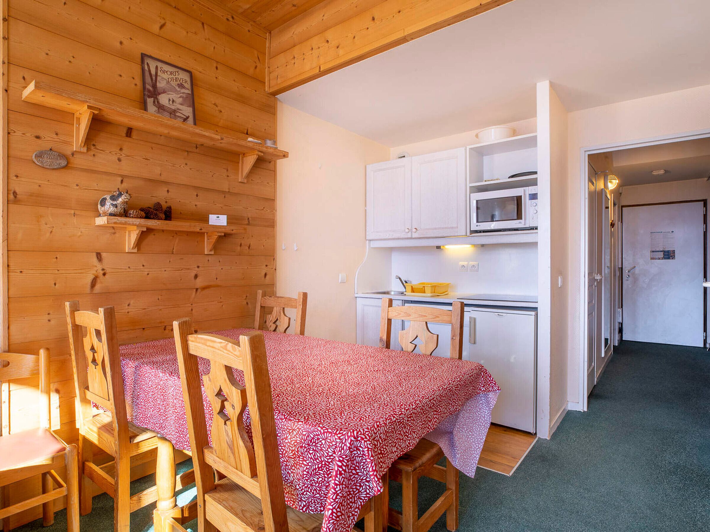 En inredning i trä med ett matbord, stolar, ett köksområde med vita skåp, en mikrovågsugn och en dörr med en skylt.
