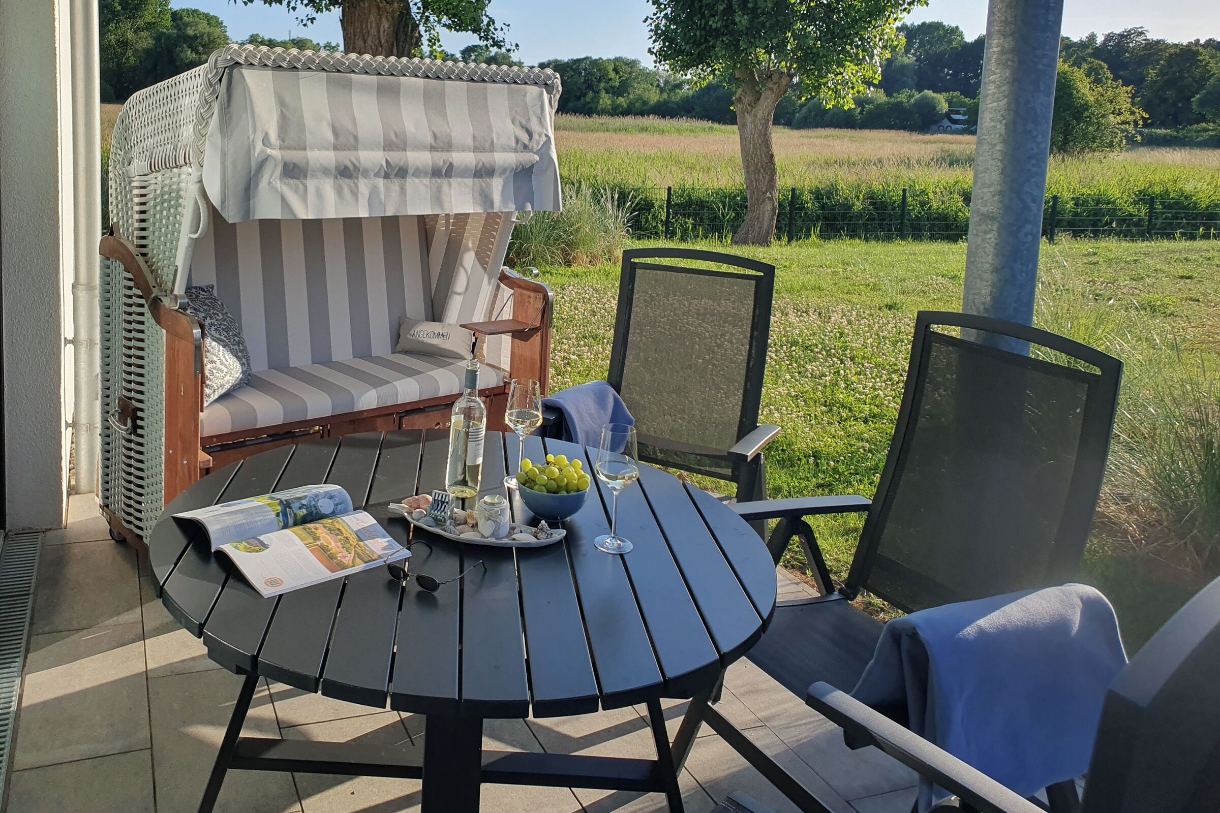A patio with a round table, chairs, a cushioned chair, and a view of a green field.