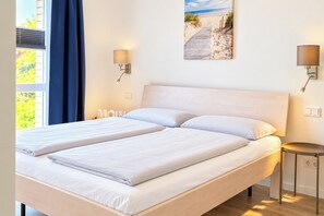 A double bed with white bedding, a small bedside table, and two wall-mounted lamps.