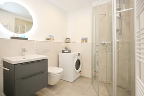 Un baño moderno con lavamanos, inodoro, lavadora y cabina de ducha de vidrio.