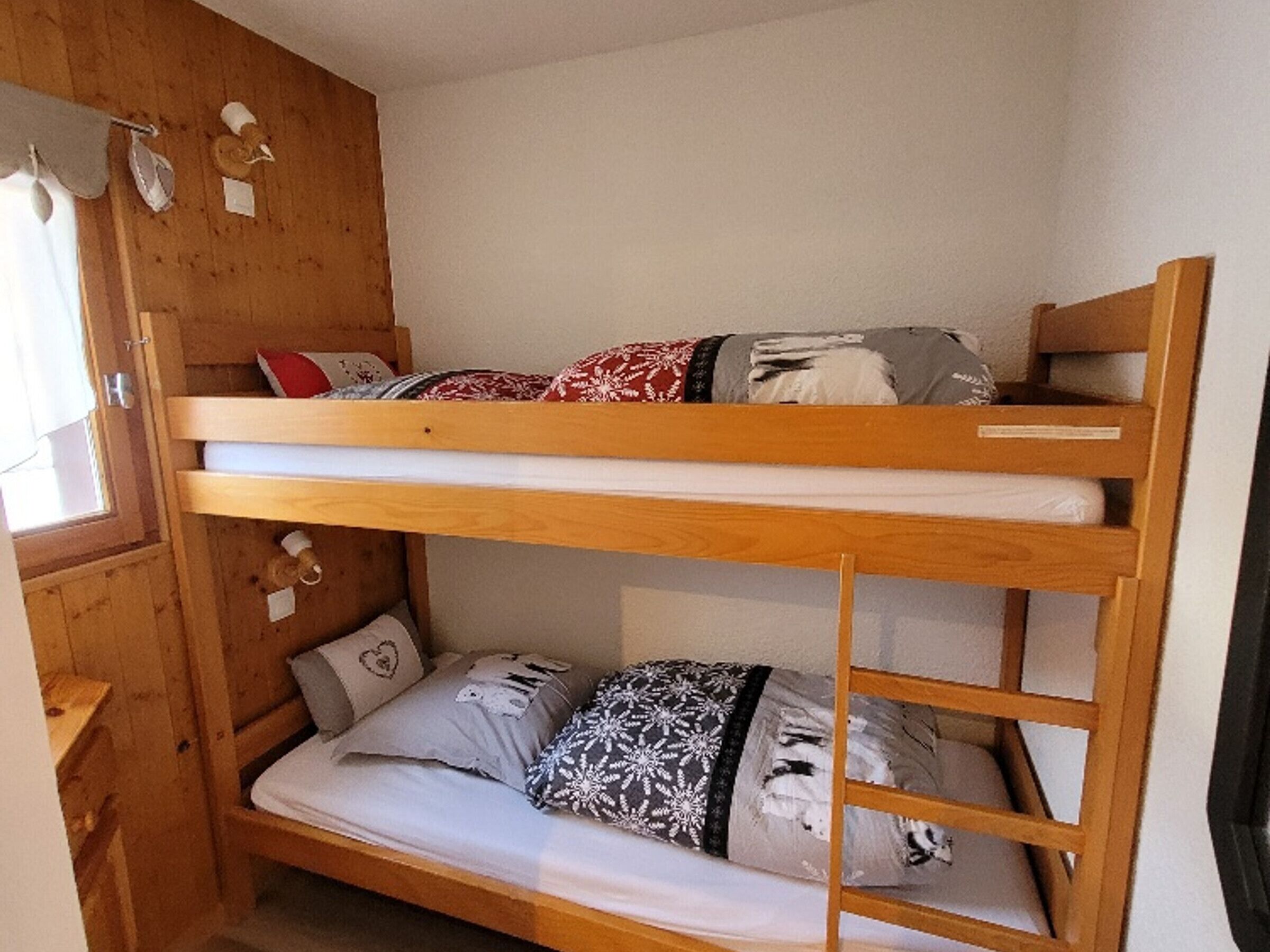 A bunk bed with two levels, wooden walls, and a window with curtains.