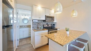 A modern kitchen with white cabinets, a granite countertop, a microwave, a stove, and two pendant lights. - FB Terrace Studio! Inquire for Monthly Rates (Panama City Beach)