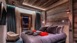 Quarto moderno com uma cama grande, uma cadeira e teto de madeira.