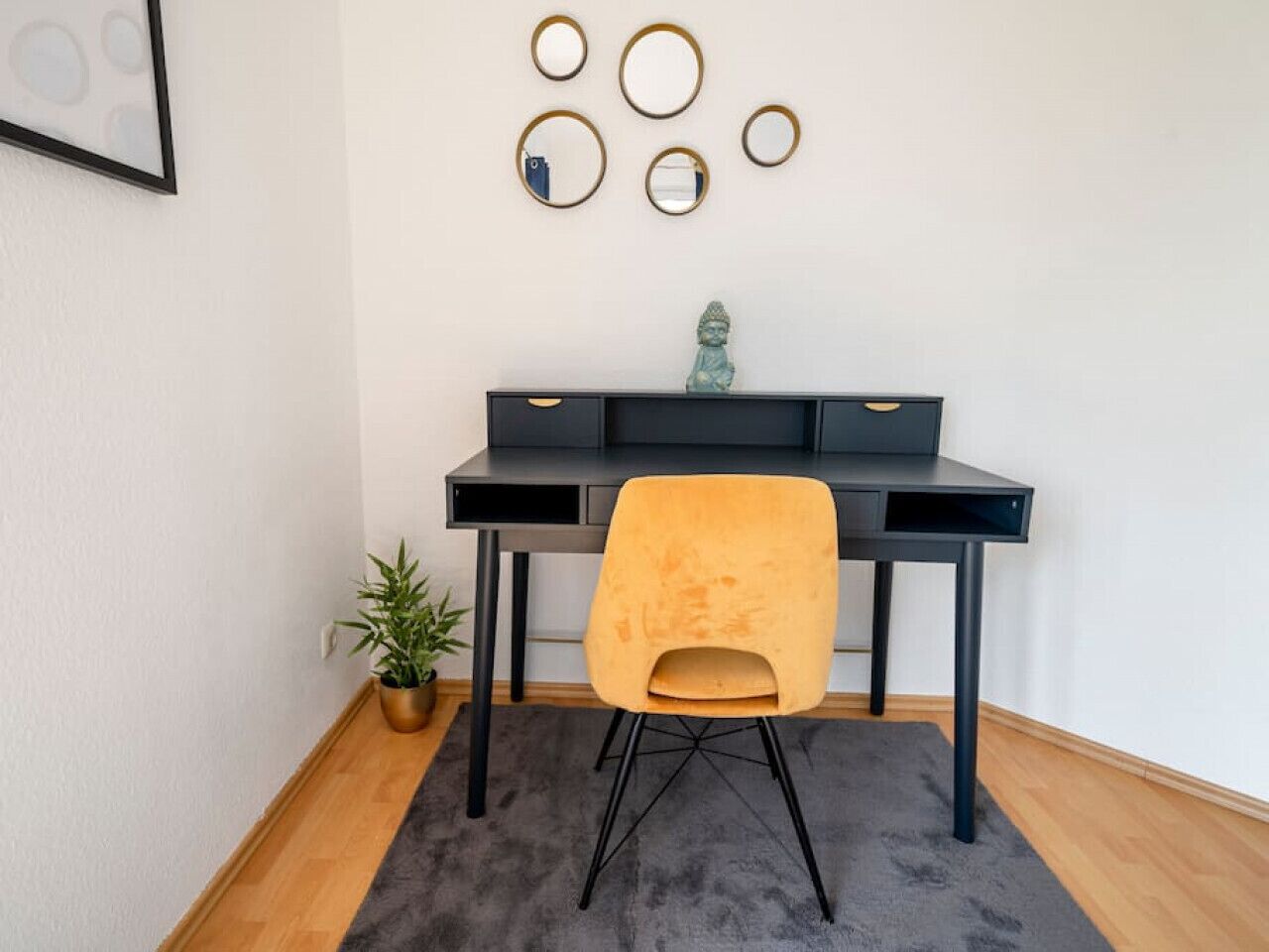 A modern desk with a black frame, a yellow chair, and a small potted plant.