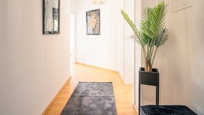 A hallway with a wooden floor, a dark rug, a potted plant, and framed pictures on the walls. - Penthouse-Suite near University (Gießen)