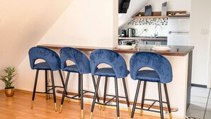 A kitchen with a bar area, featuring a modern design with a white countertop, black and gold chairs, and a potted plant. - Penthouse-Suite near University (Gießen)
