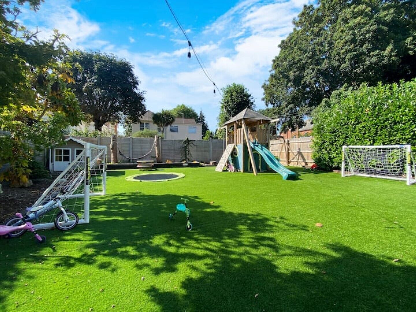 Un patio trasero con área de juegos que incluye un tobogán, un columpio y una pequeña canasta de baloncesto.