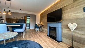 A modern living room with a fireplace, a dining area, and a kitchen in the background. - Willkommen in der Gemütlichen Ferienwohnung Bergidyll (Oberstaufen)