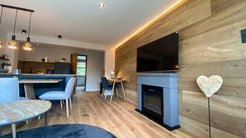 A modern living room with a fireplace, a dining area, and a kitchen in the background.