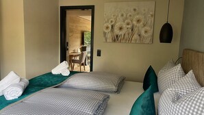 A hotel room with two beds, checkered bedding, a green pillow, a painting of flowers, and a view of the outdoors. - Willkommen in der Gemütlichen Ferienwohnung Bergidyll (Oberstaufen)