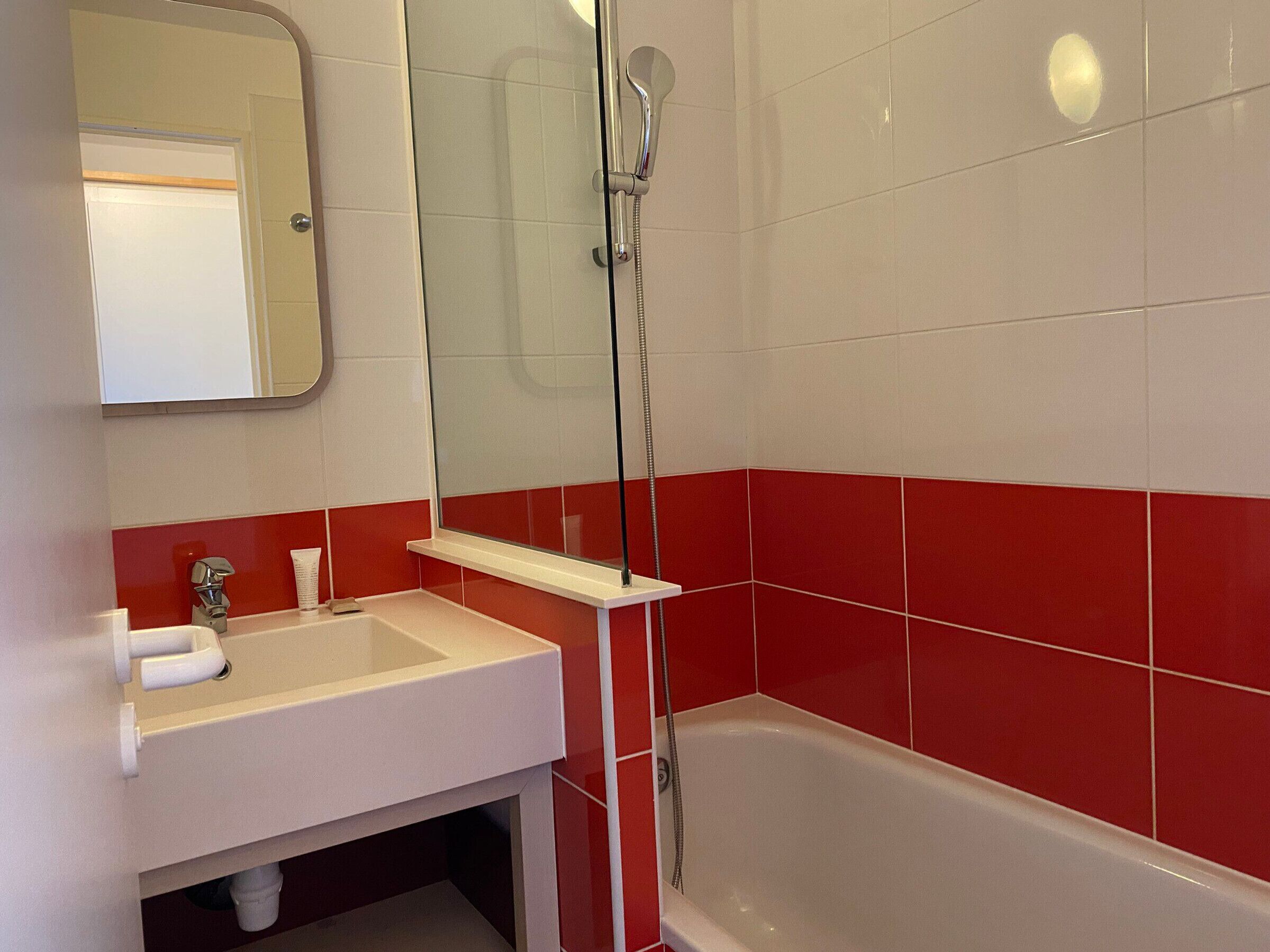 A bathroom with a white sink, red-tiled walls, a glass-enclosed shower, and a mirror above the sink.