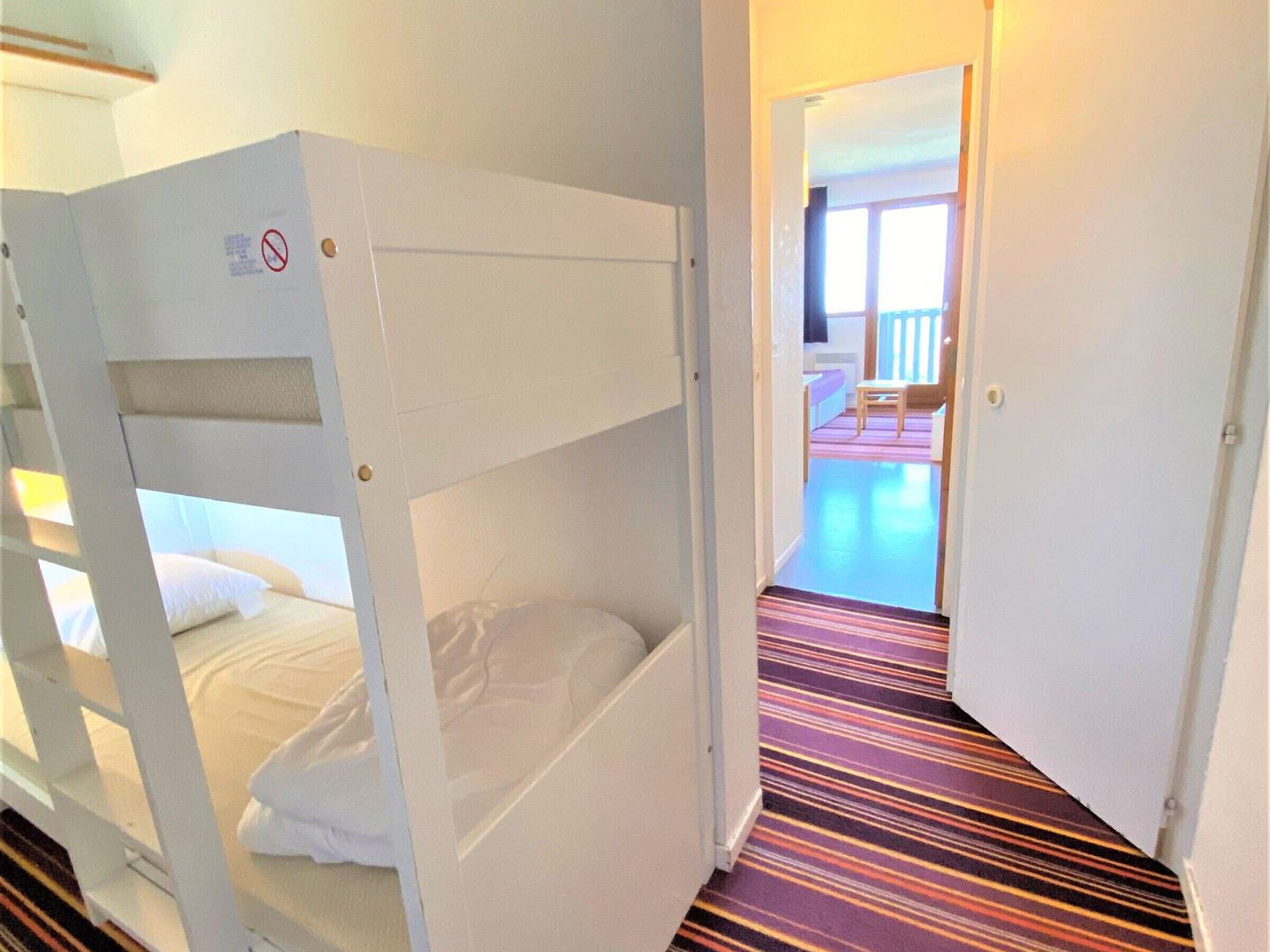 A bunk bed room with a striped carpet and a door leading to a balcony.