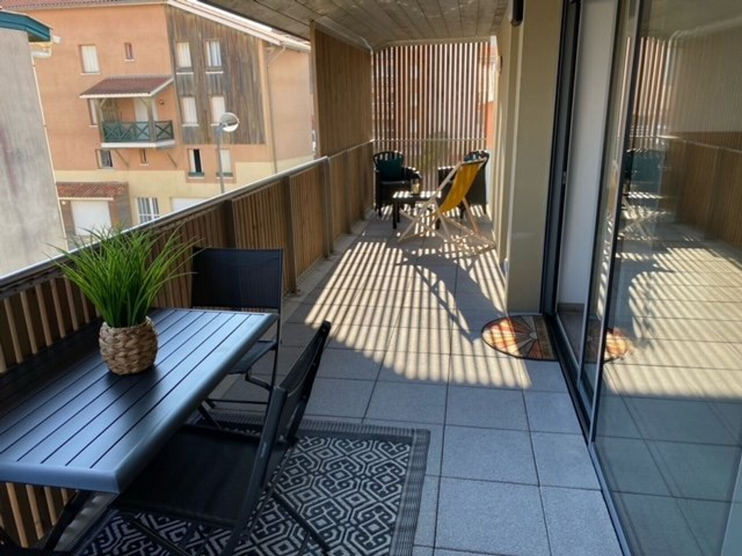 A balcony with a table and chairs, a potted plant, and a patterned rug.