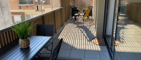 A balcony with a table and chairs, a potted plant, and a patterned rug.