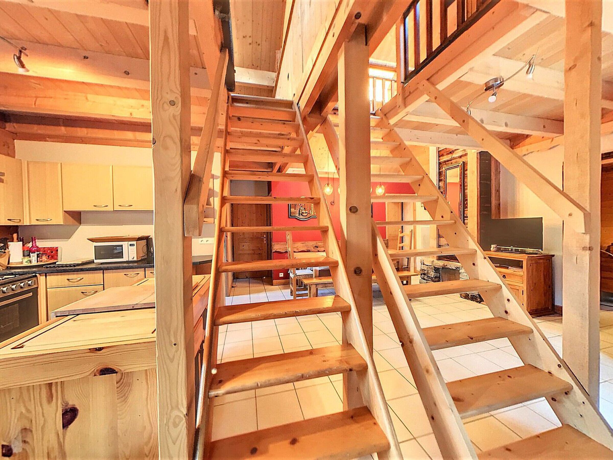 A wooden staircase leading to a second floor in a cabin-style interior with a kitchen area visible.