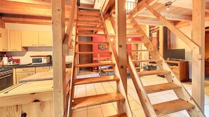 A wooden staircase leading to a second floor in a cabin-style interior with a kitchen area visible. - Comfortable 3-star apartment, large terrace and private parking (Le Corbier)