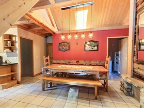 A dining area with a wooden table and benches, a red wall with framed pictures, and a ceiling with exposed beams.