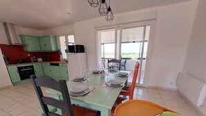 A dining area with a table set for four, kitchen cabinets, and a view through the glass door. - Charming Countryside Retreat with Modern Amenities, Babyfoot, and Nearby Leisure Activities (Saint-Erblon)