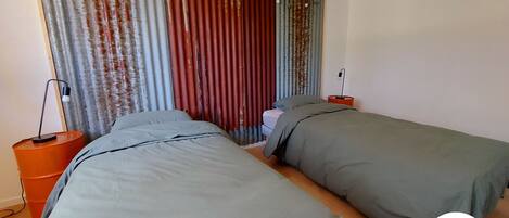 Een slaapkamer met twee bedden, een nachtkastje, een lamp en een gordijn met een lichtslingering.