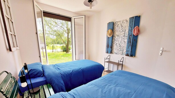 A room with two beds, a window with a view of greenery, a wall-mounted hat rack, and a ceiling light. - Charming Countryside Retreat with Modern Amenities, Babyfoot, and Nearby Leisure Activities (Saint-Erblon)