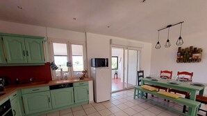 A kitchen with green cabinets, a dishwasher, and a dining area with a table set for four. - Charming Countryside Retreat with Modern Amenities, Babyfoot, and Nearby Leisure Activities (Saint-Erblon)
