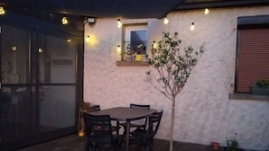 A wooden deck with a table and chairs, a potted tree, and string lights. - Charming Countryside Retreat with Modern Amenities, Babyfoot, and Nearby Leisure Activities (Saint-Erblon)