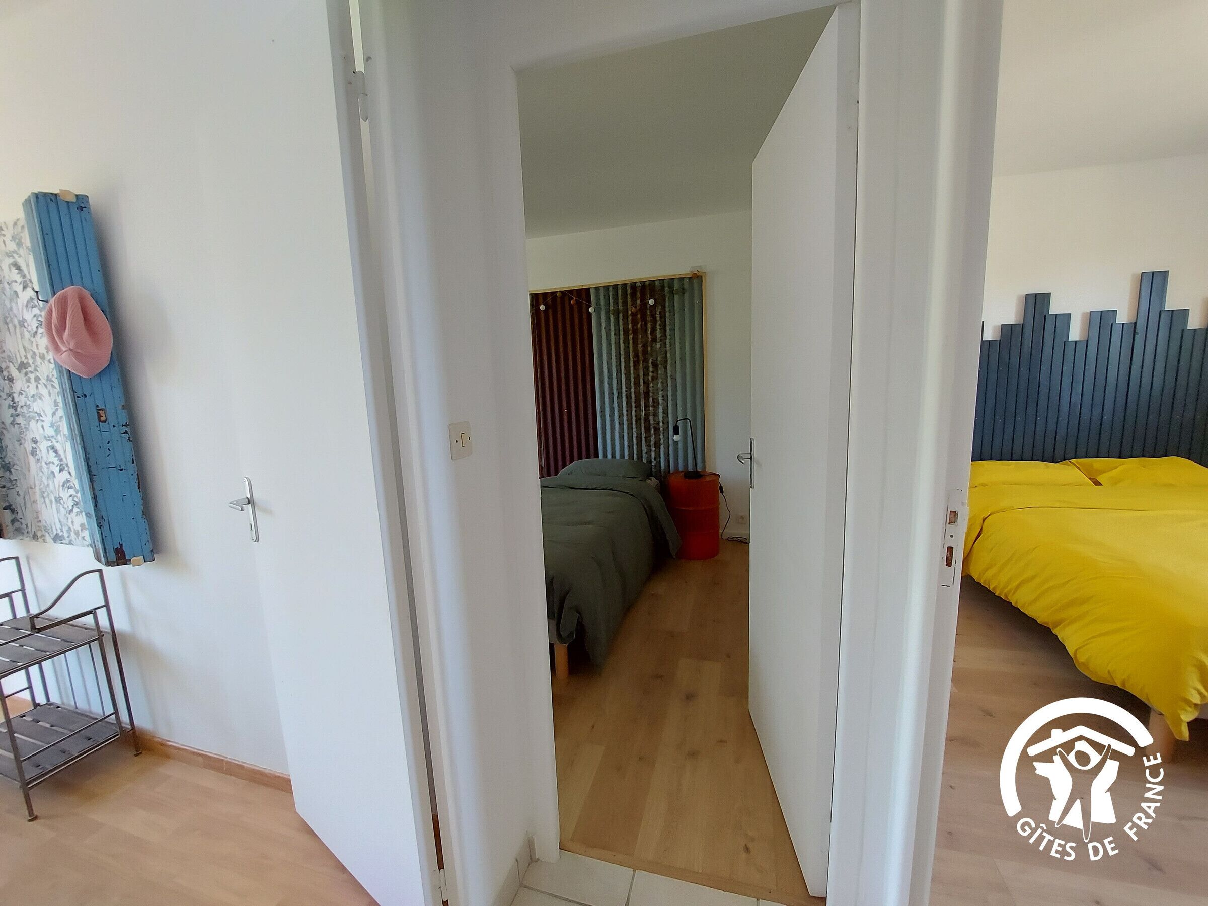 A room with a bed, a wardrobe, a red bucket, and a metal shelf unit.