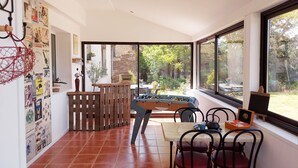 A room with a foosball table, a dining table with chairs, a window with a view of greenery, and a wall with various posters. - Charming Countryside Retreat with Modern Amenities, Babyfoot, and Nearby Leisure Activities (Saint-Erblon)