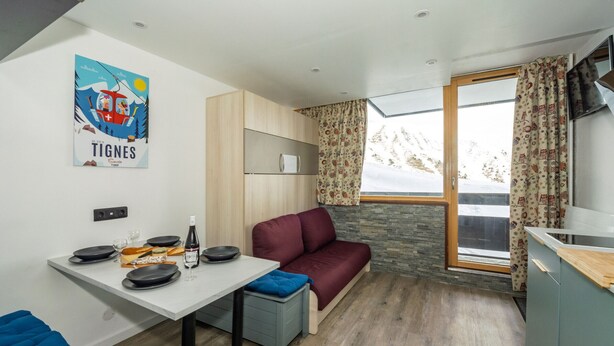 A compact living space with a dining table, a sofa, a small kitchen area, and a window with curtains. - Comfortable studio ski-in/out with balcony and WIFI (Tignes)