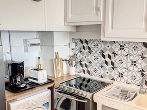 A compact kitchen with a washing machine, a coffee maker, a toaster, an oven, and a sink with a dish rack.
