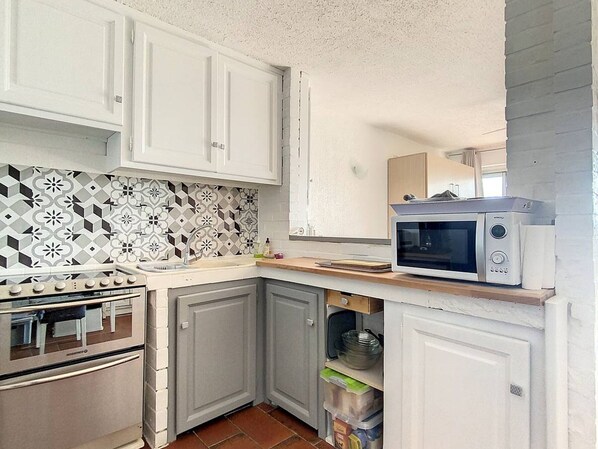 A compact kitchen with white cabinets, a patterned backsplash, a microwave, and a stove.