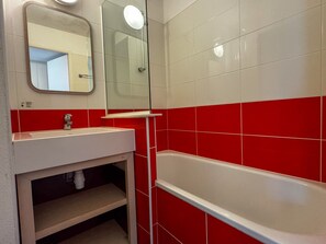 Un bagno con un lavandino bianco, uno specchio e una vasca da bagno su piastrelle rosse.