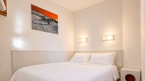 Et hotelværelse med en stor seng, et billede på væggen, to vægmonterede lamper og en lille højttaler.