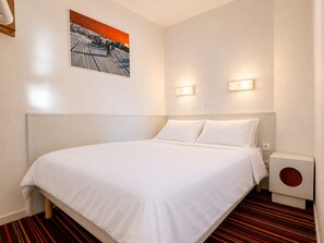Una camera d'albergo con un letto grande, un quadro appeso al muro, due luci a parete e un piccolo altoparlante.