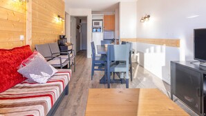 A modern interior with a sofa, dining table, and chairs, wooden walls, and a kitchen area.