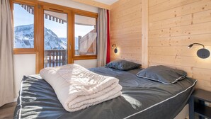 A bedroom with a bed, wooden walls, a window with a view of mountains, and a nightstand.