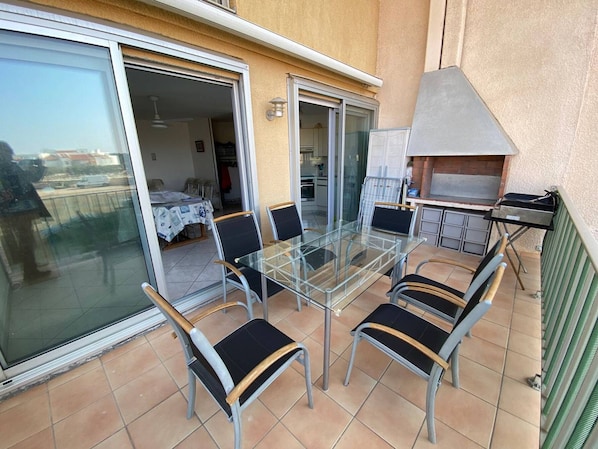 A glass-top dining table with chairs, a sliding glass door leading to a balcony, and a grill outside.