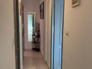 A narrow hallway with a door on the right, a door on the left, and a small shelf with books and a decorative item in the center.